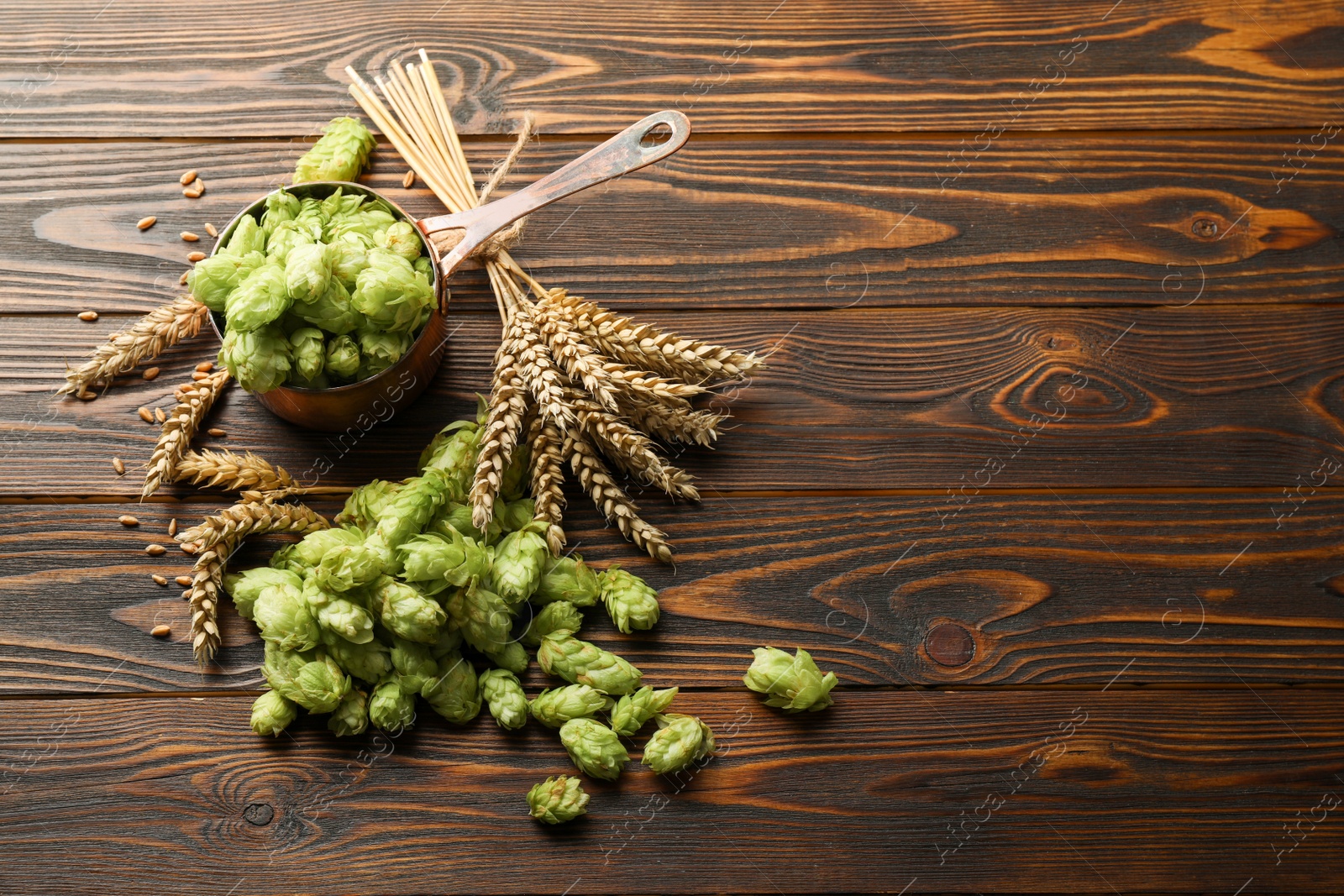 Photo of Fresh hop flowers and wheat ears on wooden table, space for text