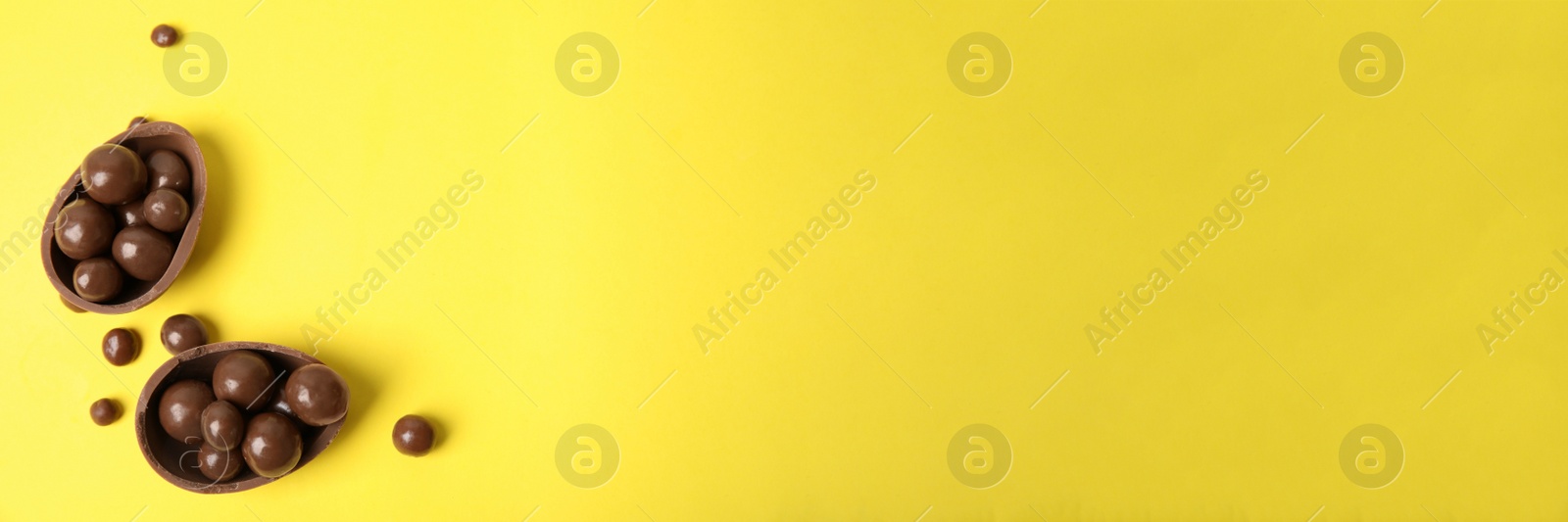 Image of Tasty chocolate egg and candies on yellow background, flat lay with space for text. Banner design