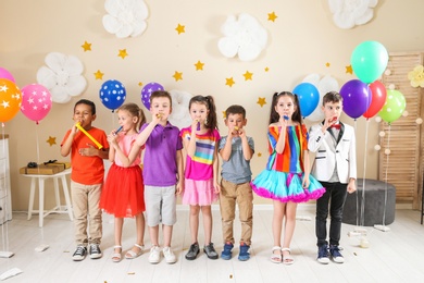 Photo of Adorable children with party blowers indoors. Birthday celebration