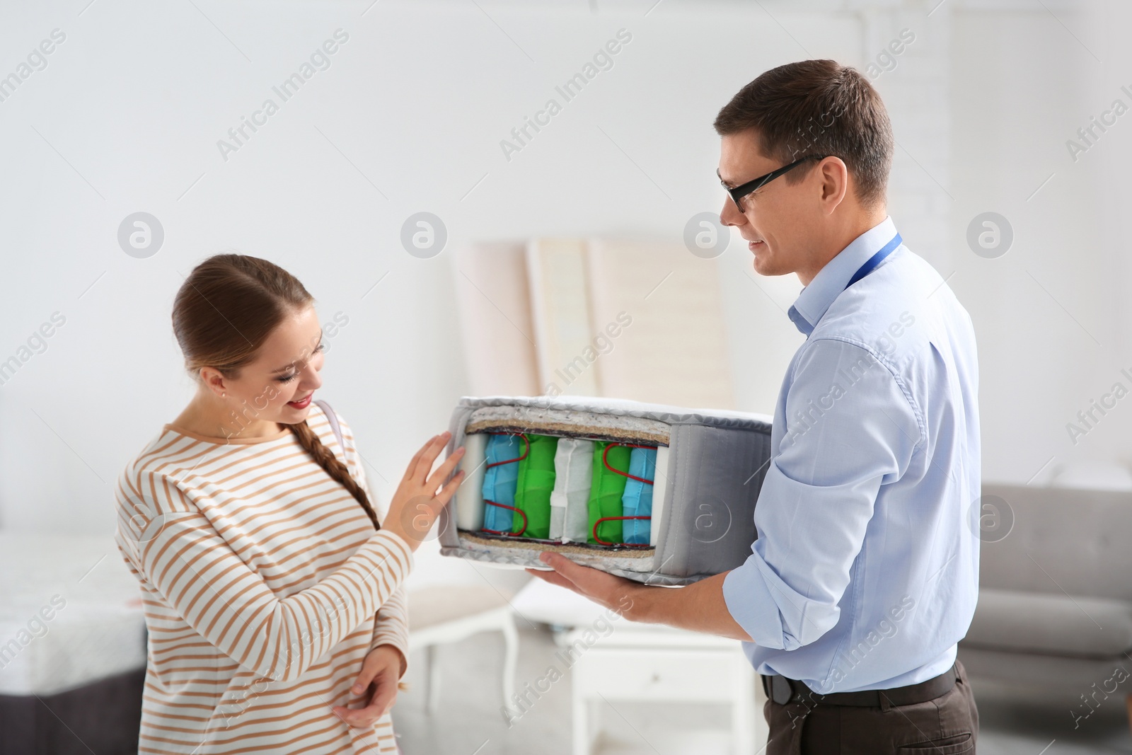 Photo of Salesman showing young woman section of mattress in store