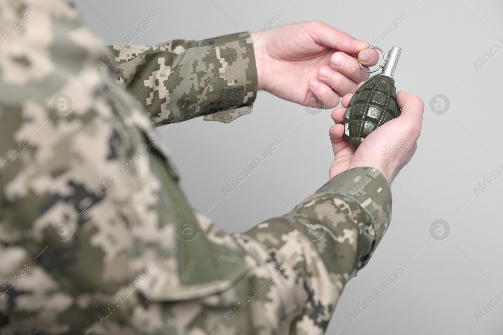 Photo of Soldier pulling safety pin out of hand grenade on light grey background, closeup. Military service