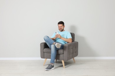 Happy man sitting in armchair and using smartphone indoors