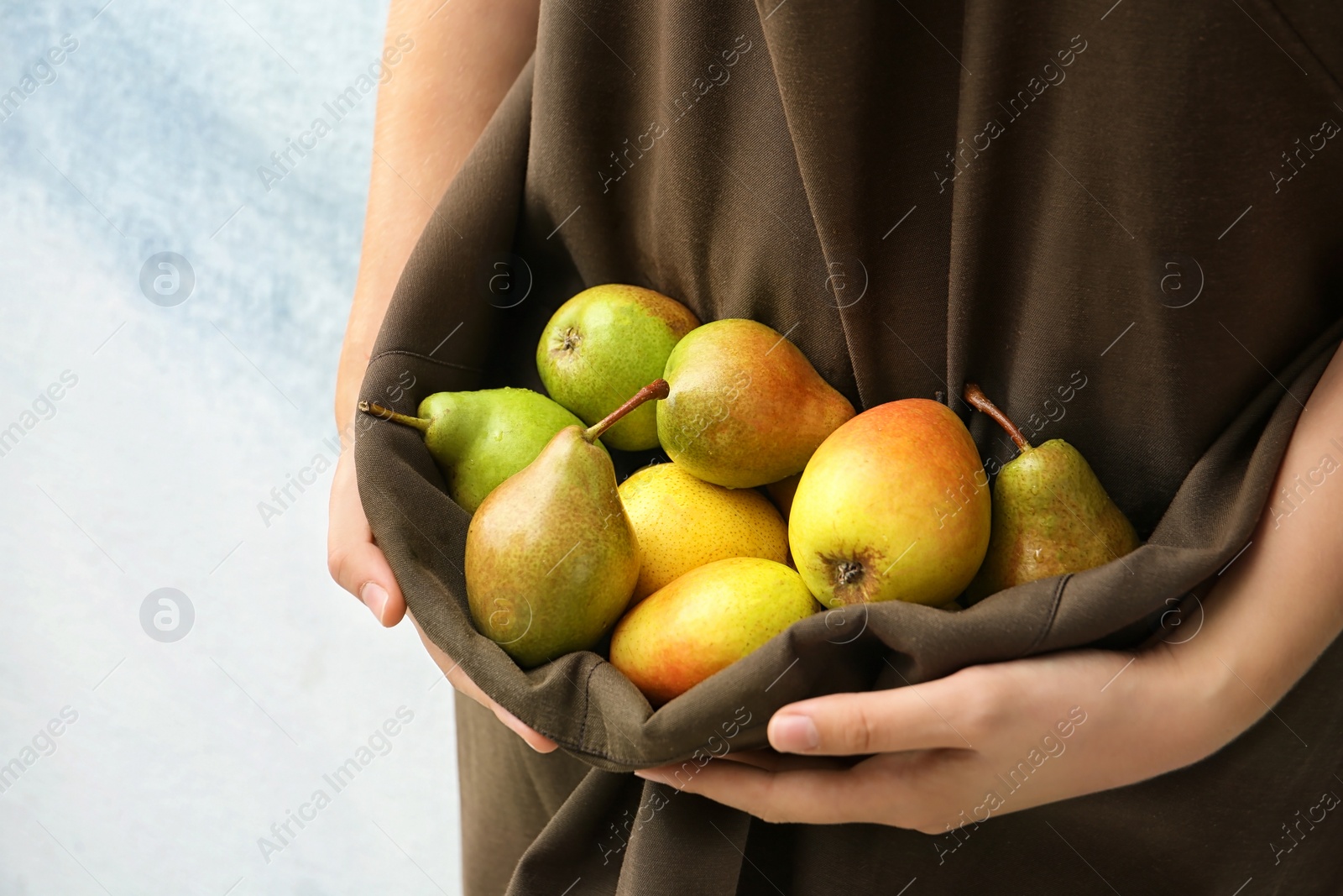 Photo of Woman in apron with ripe pears on color background, closeup