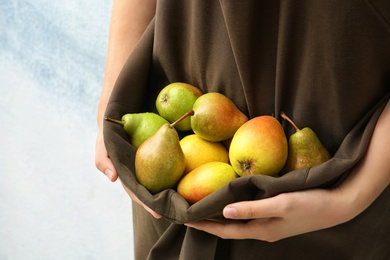 Woman in apron with ripe pears on color background, closeup