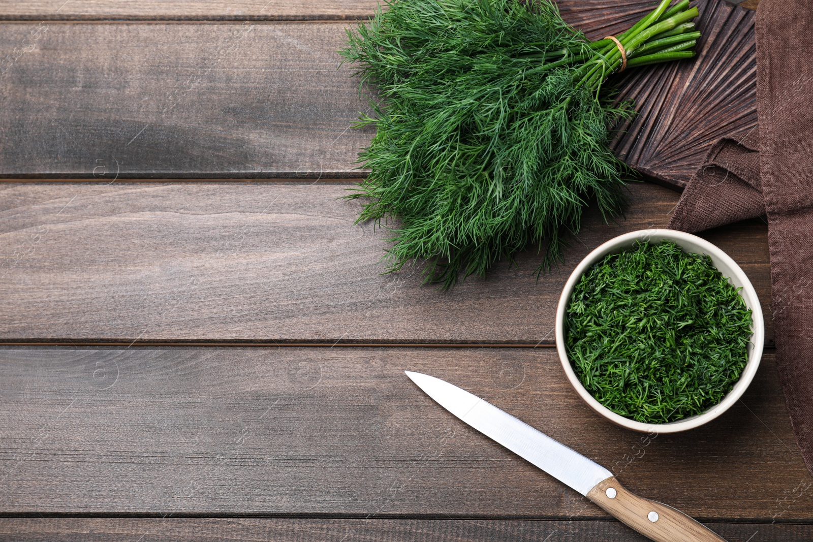 Photo of Fresh dill, knife and napkin on wooden table, flat lay. Space for text