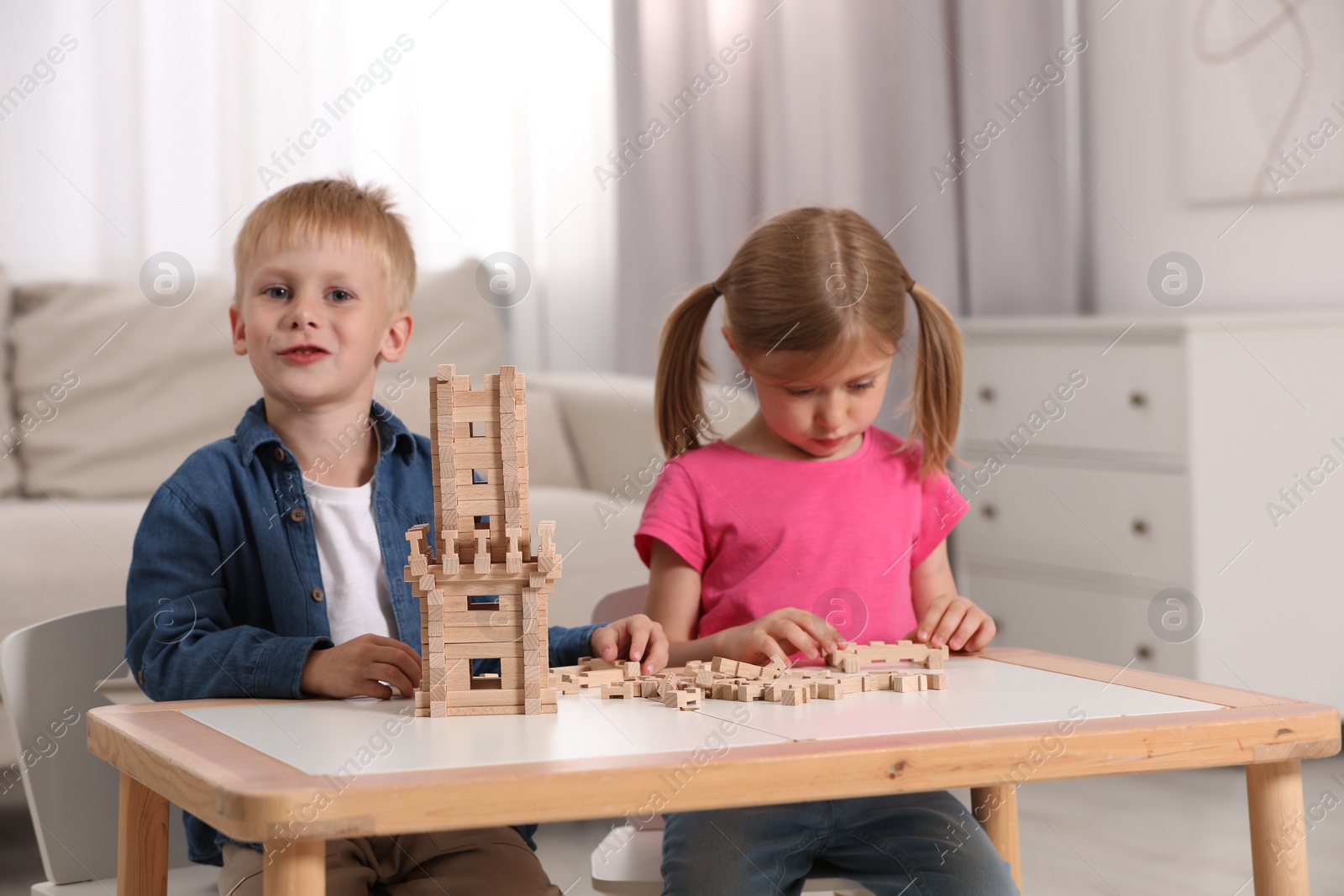 Photo of Little girl and boy playing with wooden tower at table indoors. Children's toy