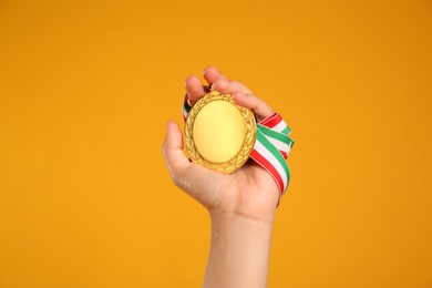 Photo of Woman holding gold medal on yellow background, closeup