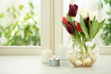 Photo of Beautiful tulips in glassware and candles on window sill. Space for text