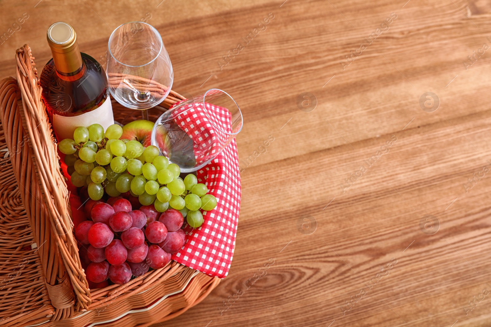 Photo of Picnic basket with wine, glasses and grapes on wooden table. Space for text