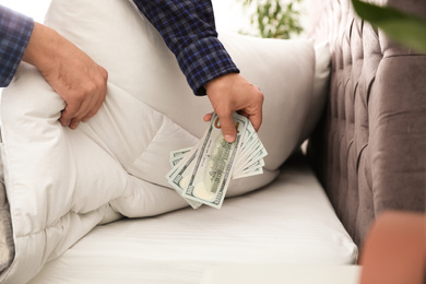 Photo of Man hiding dollar banknotes under blanket in bedroom, closeup. Money savings