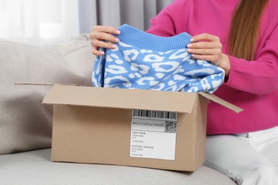 Photo of Woman unpacking parcel on sofa at home, closeup. Online store