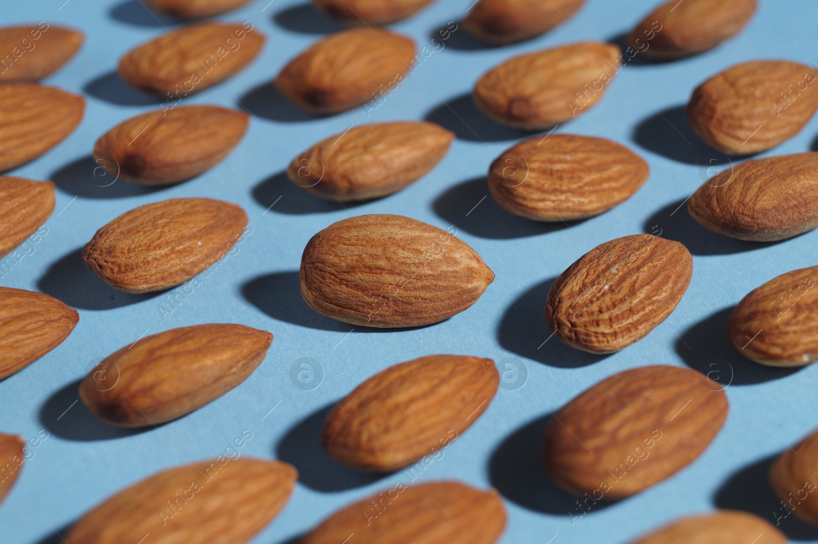 Photo of Delicious raw almonds on light blue background, closeup