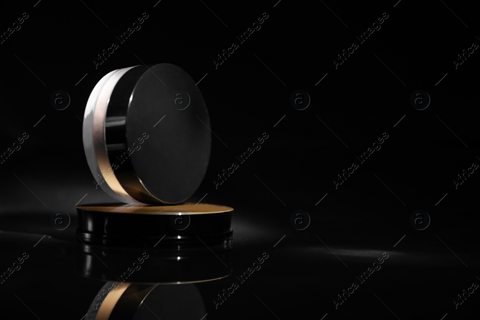 Photo of Jars of face powders on black mirror surface in darkness, closeup. Space for text