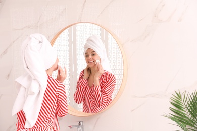 Photo of Young woman with towel on head near mirror in bathroom