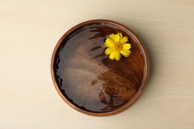Water with flower in bowl on wooden table, top view