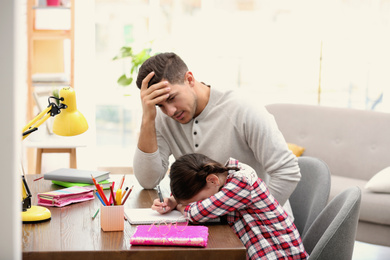 Photo of Upset father and daughter doing homework together at table indoors