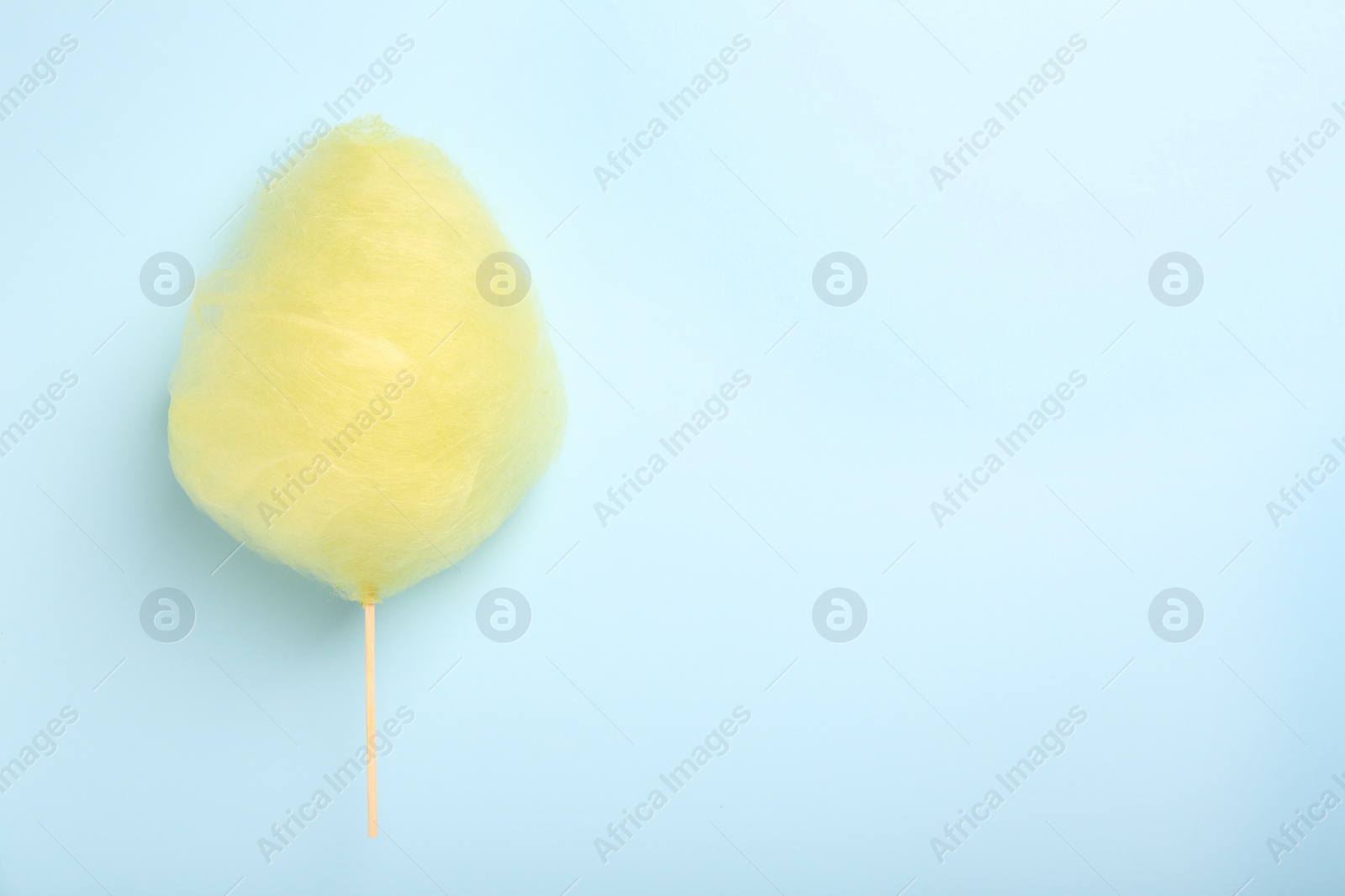 Photo of One sweet yellow cotton candy on light blue background, top view. Space for text