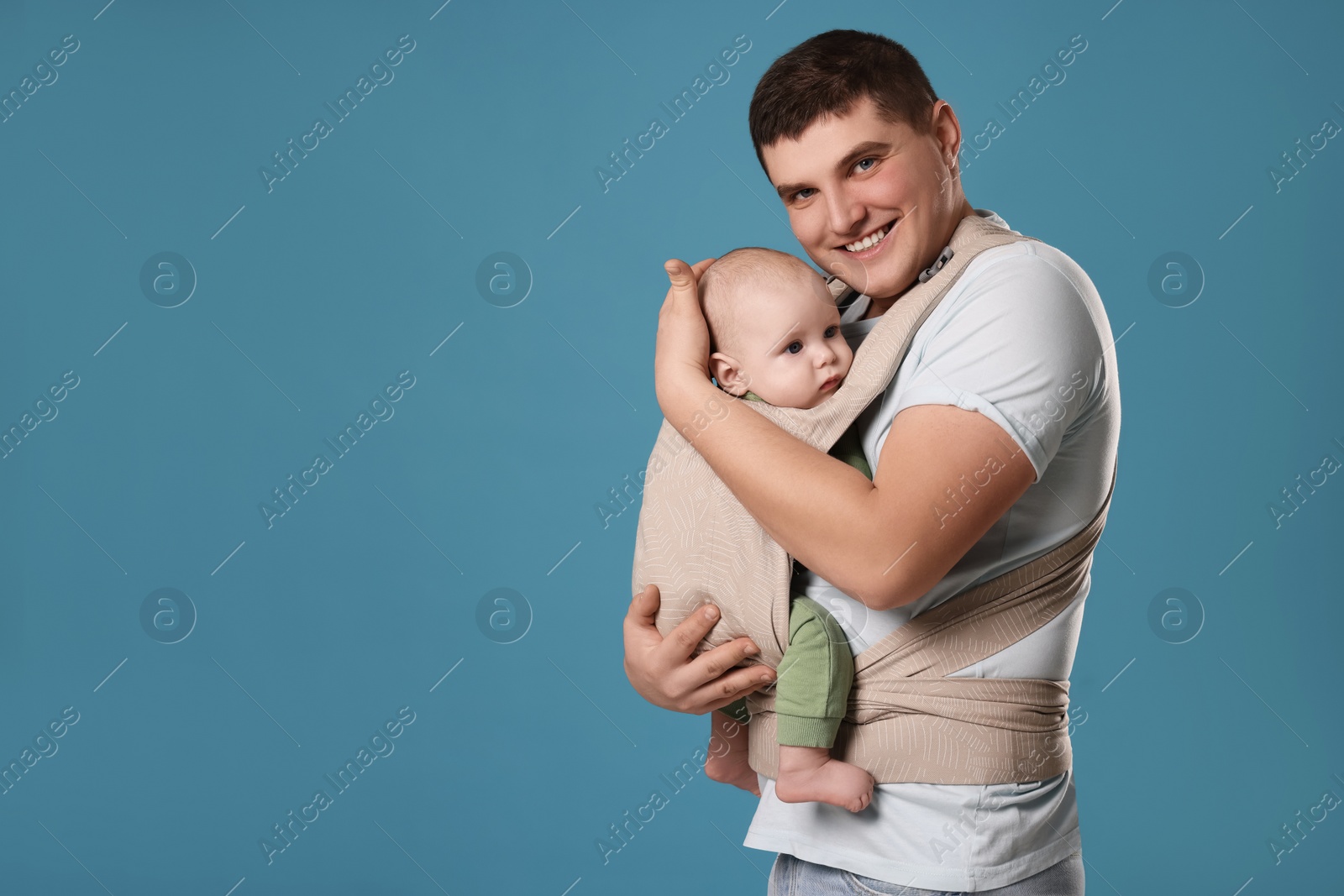 Photo of Father holding his child in sling (baby carrier) on light blue background. Space for text