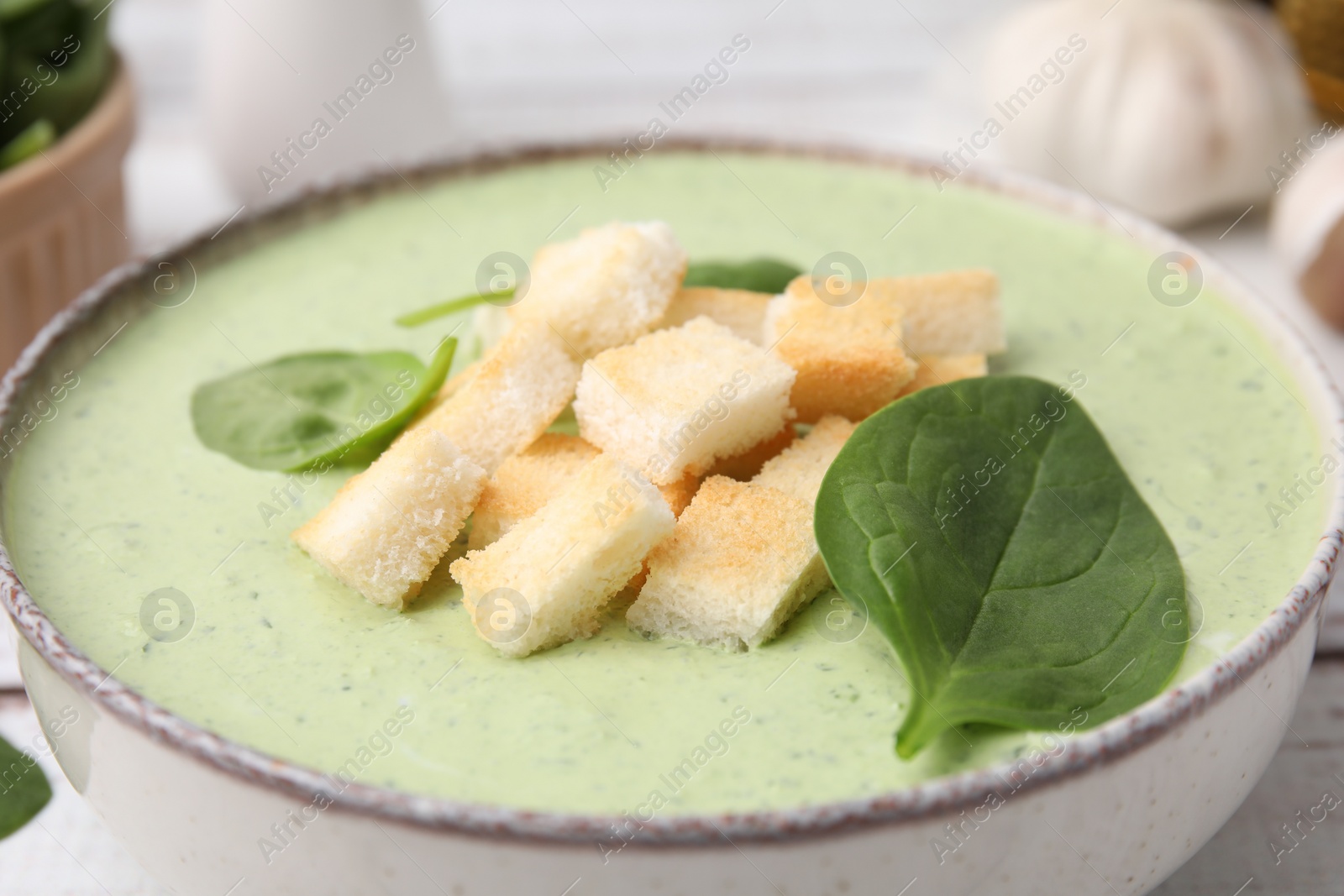 Photo of Delicious spinach cream soup with leaves and croutons in bowl on table, closeup