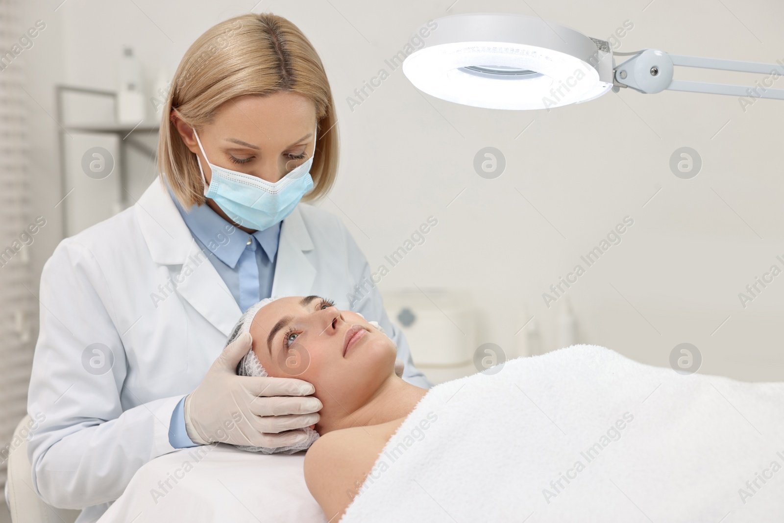 Photo of Dermatologist examining patient`s face under lamp in clinic