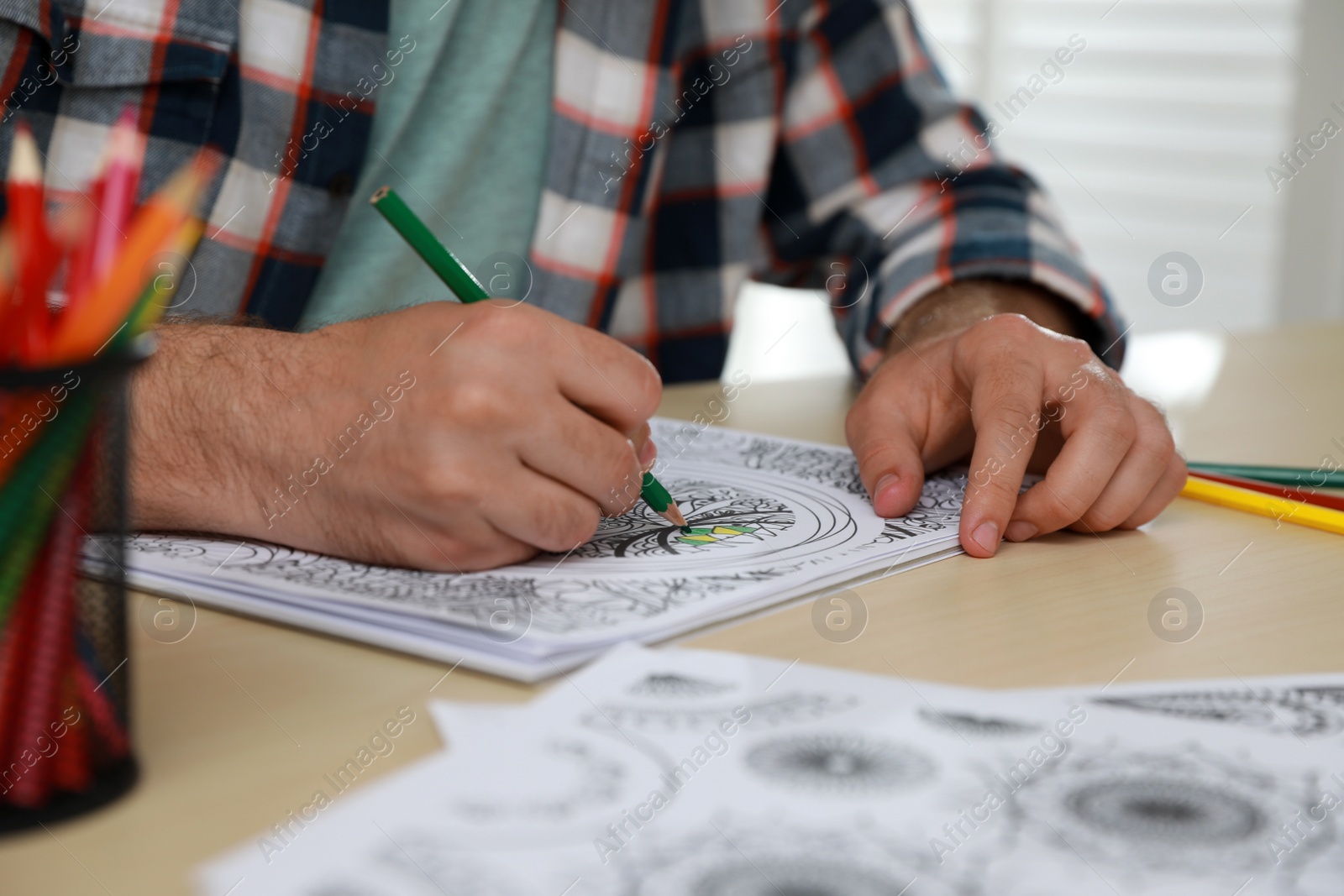 Photo of Man coloring antistress picture at table indoors, closeup