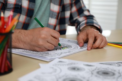 Photo of Man coloring antistress picture at table indoors, closeup