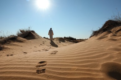 Man in arabic clothes walking through desert on sunny day, back view