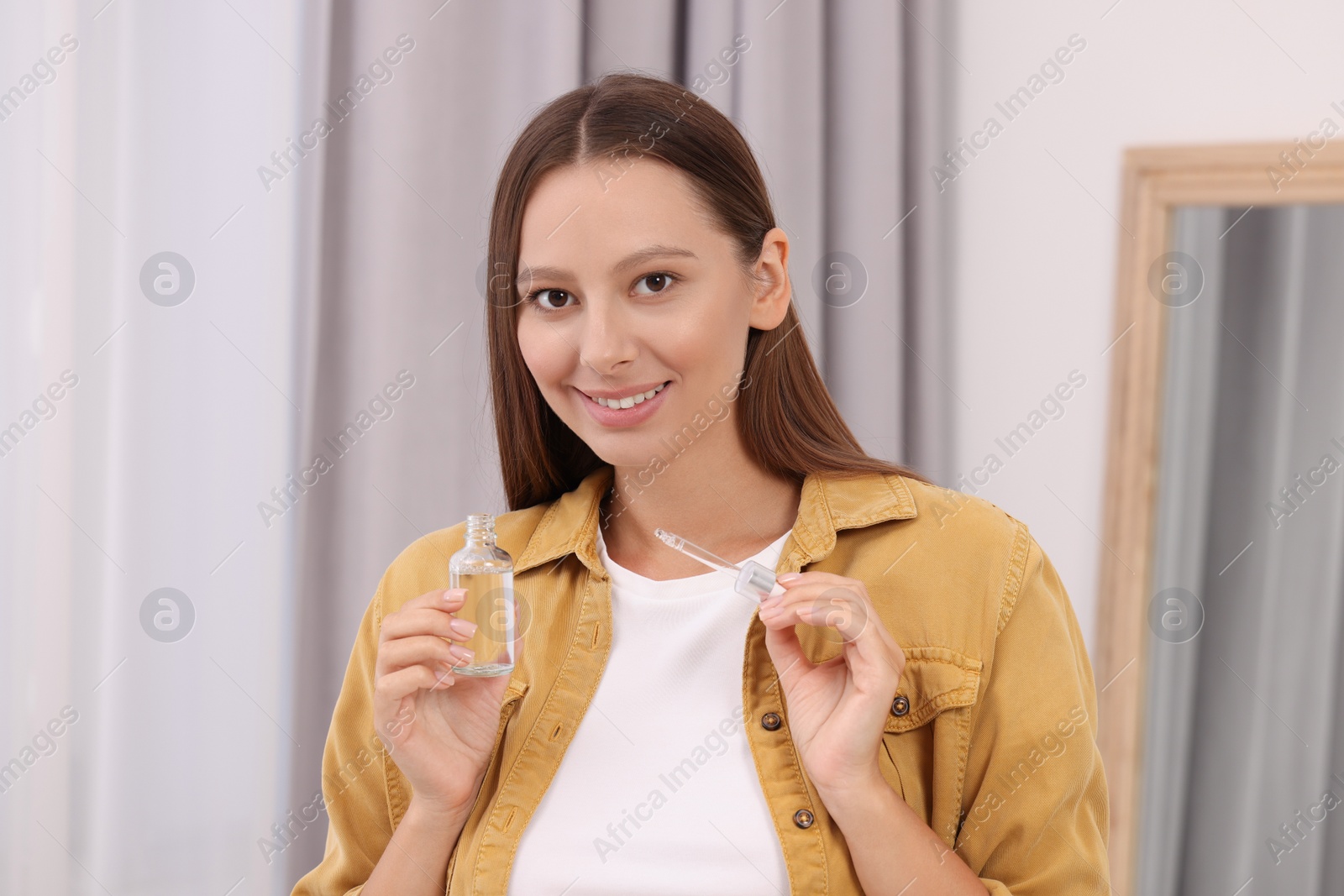 Photo of Beautiful woman with bottle of serum and dropper indoors