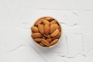Photo of Tasty almonds in wooden bowl on white textured table, top view