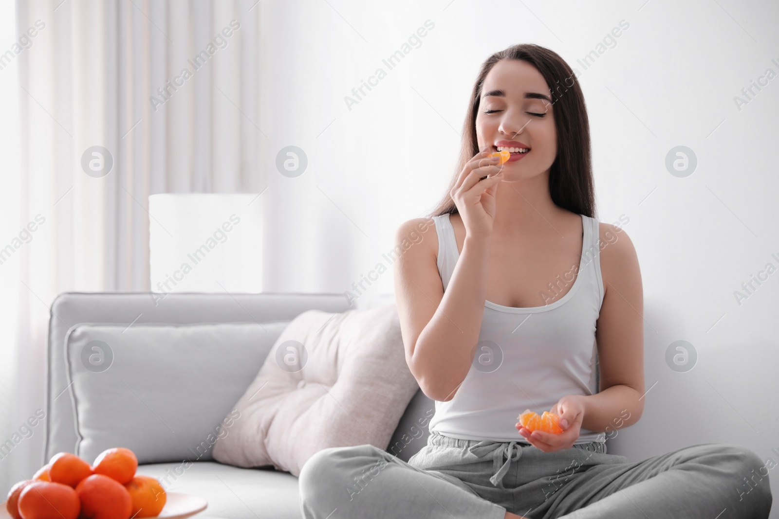 Photo of Happy young woman eating ripe tangerine at home