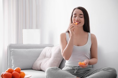 Photo of Happy young woman eating ripe tangerine at home