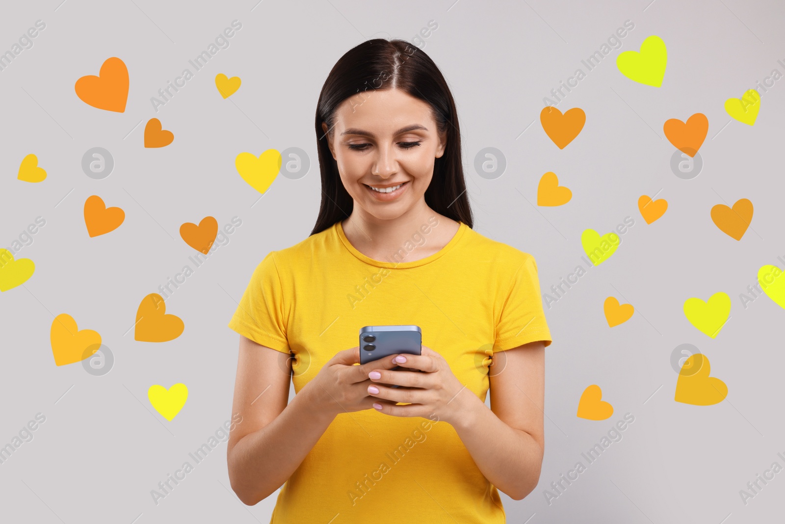 Image of Long distance love. Woman chatting with sweetheart via smartphone on grey background. Hearts flying out of device and swirling around her