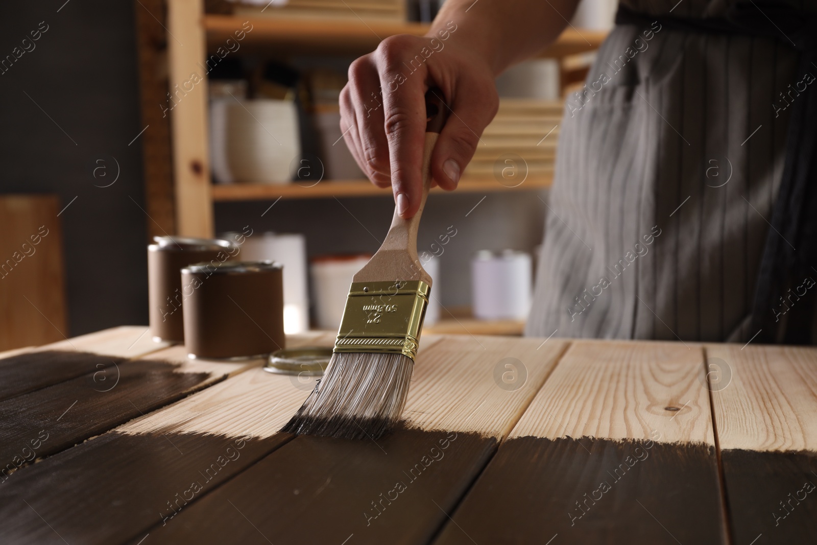 Photo of Man with brush applying wood stain onto wooden surface indoors, closeup