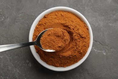 Photo of Taking cinnamon powder with spoon from bowl on grey table, top view