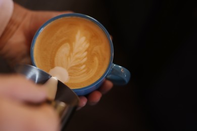 Barista pouring milk into cup of coffee on black background, closeup. Space for text