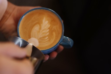 Photo of Barista pouring milk into cup of coffee on black background, closeup. Space for text