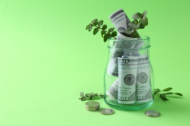 Financial savings. Dollar banknotes in glass jar, twigs and coins on green background, space for text