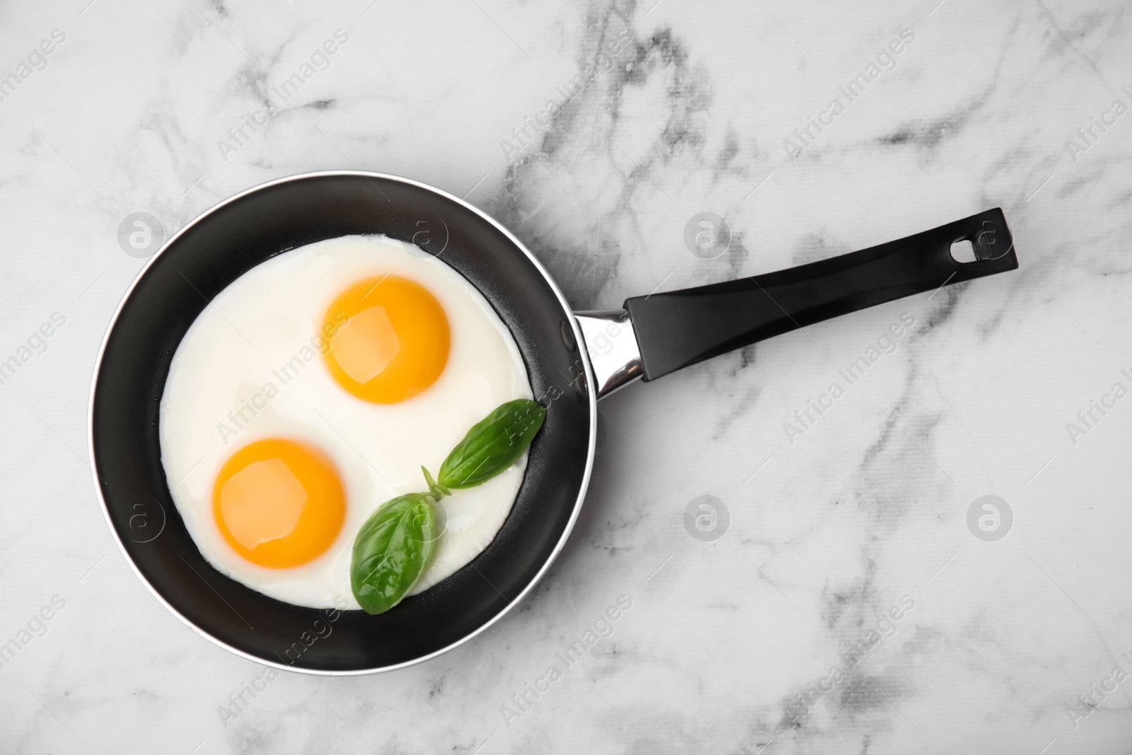 Photo of Tasty fried eggs with basil in pan on white marble table, top view. Space for text
