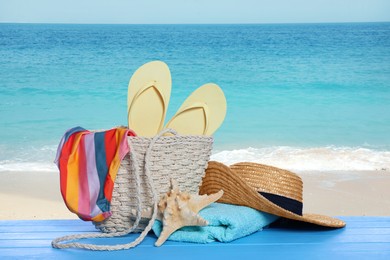 Image of Stylish bag and other beach accessories on light blue wooden table near sea