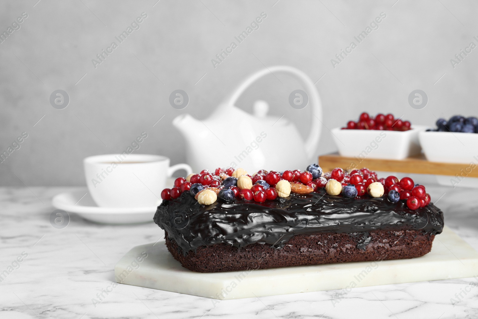 Photo of Delicious chocolate sponge cake with berries and nuts on white marble table