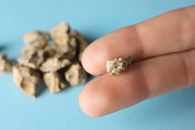Photo of Woman holding kidney stone above light blue background, closeup. Space for text