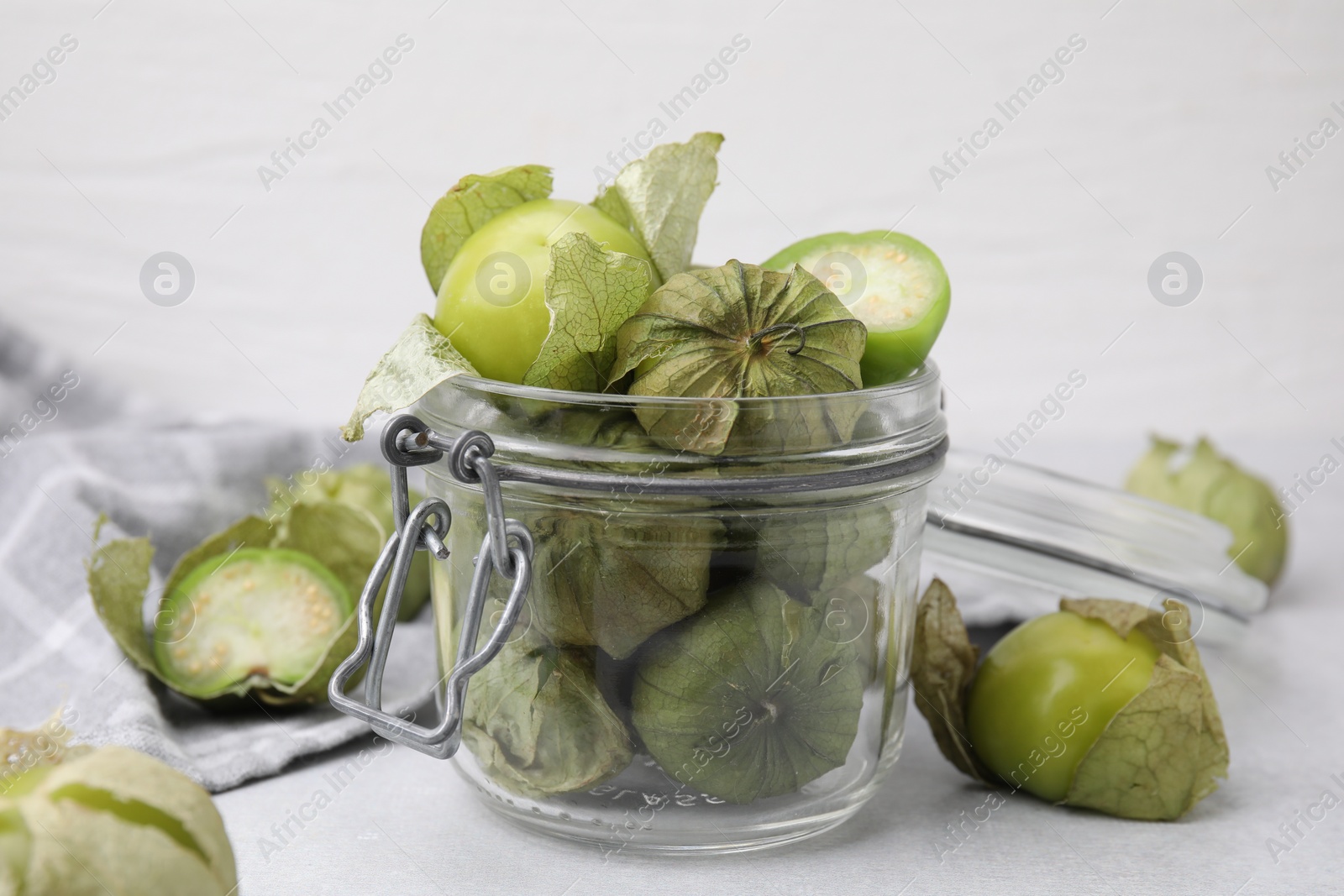 Photo of Fresh green tomatillos with husk in glass jar on light table, closeup