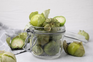 Fresh green tomatillos with husk in glass jar on light table, closeup