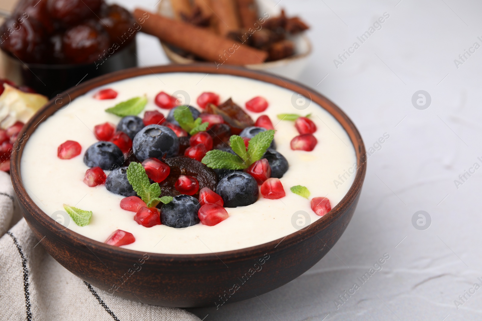 Photo of Delicious semolina pudding with blueberries, pomegranate, dates and mint in bowl on white table, closeup. Space for text