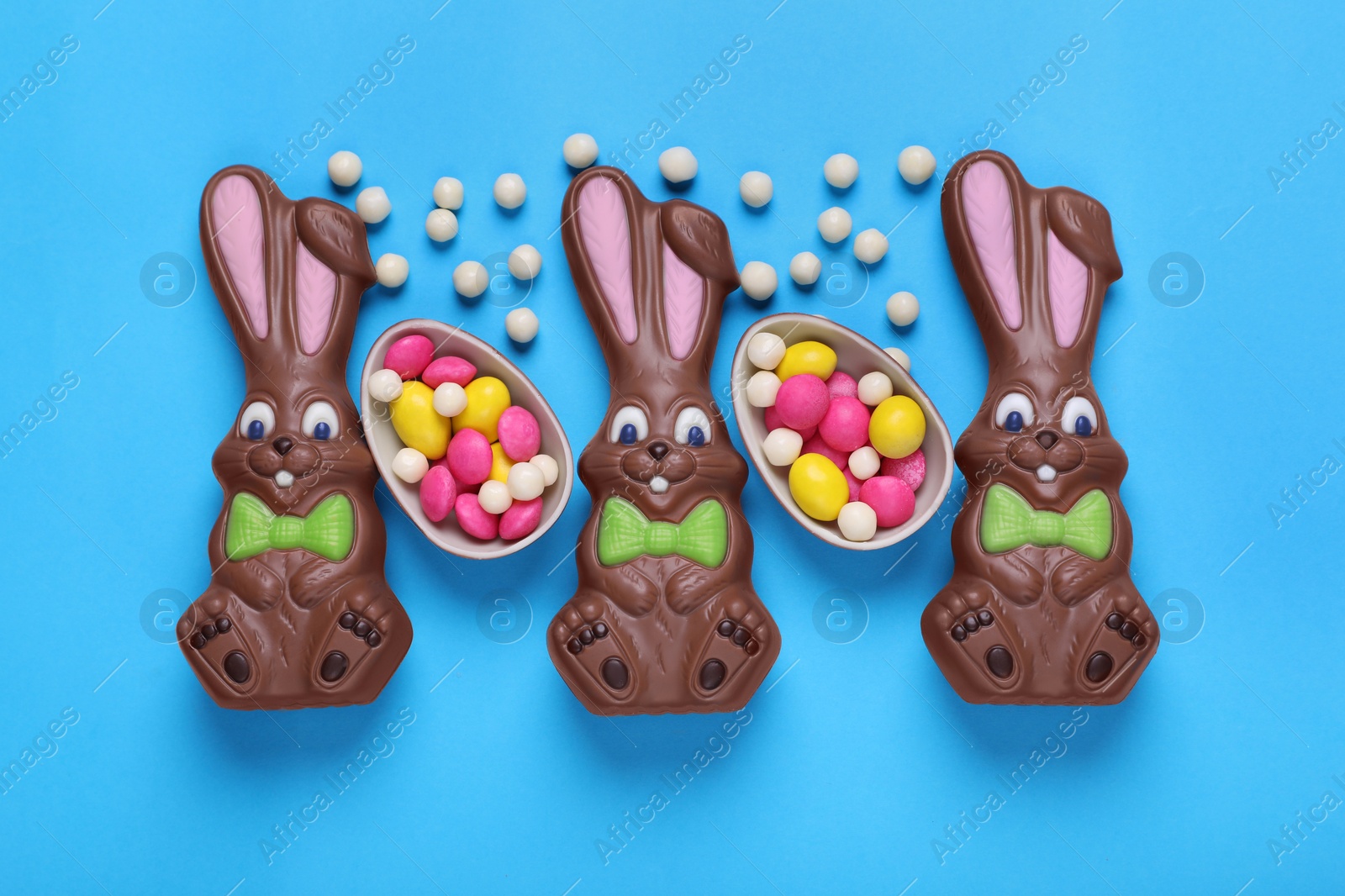 Photo of Chocolate Easter bunnies, halves of egg and candies on light blue background, flat lay