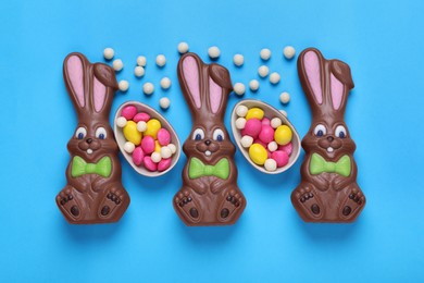 Chocolate Easter bunnies, halves of egg and candies on light blue background, flat lay