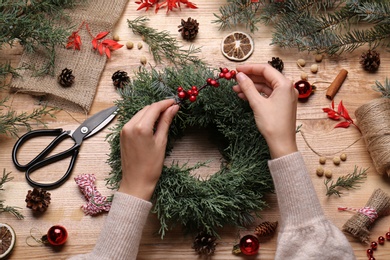 Photo of Florist making beautiful Christmas wreath with berries at wooden table, top view