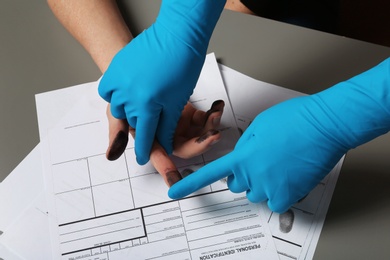 Photo of Investigator taking fingerprints of suspect on table, closeup