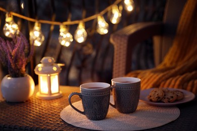 Photo of Cups with tasty cocoa on rattan table at balcony in evening