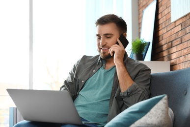 Young man talking on phone while using laptop in living room